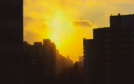 Kyiv, Ukraine. Silhouette of multistory apartment buildings on the background of yellow and orange sky at sunset. City street goes into distance over a horizon. Dense residential development, houses.の写真素材