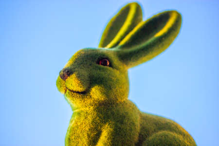 Green cute funny Easter bunny with long ears on a background of clear blue sky in springtime. Easter holiday in April. Toy decorative dreamy hare - a symbol of Easter. Smiling rabbit close-upの写真素材