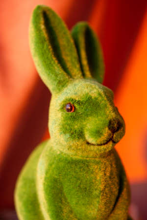 Green cute funny Easter bunny with long ears on orange brown background in springtime. Easter holiday in April. Toy decorative hare - a symbol of Easter. Smiling rabbit. vertical photography.の写真素材