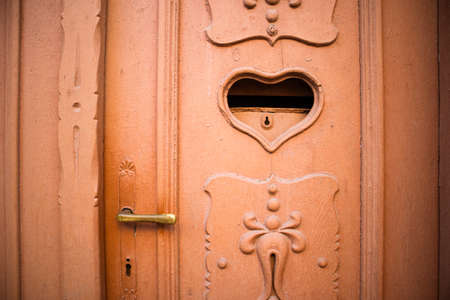 Beautiful antique terracotta door decorated with carvings and postal mail slot. Letter box in shape of heart with key hole. Valentine's day concept. Mailbox for love letters. Feeling love background.の写真素材