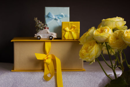 Yellow blue gift boxes stacked on dark black grey background, Austin roses bouquet. Toy retro car...