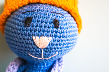 Blue crocheted knitted smiling toy cat in yellow hat with copy space. Amigurumi art. Fragment of...