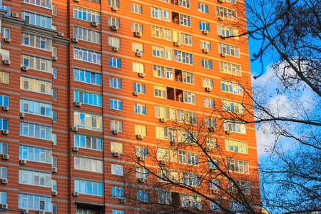 Kiev, Ukraine, January 2, 2022. Red brick wall of high-rise apartment building against a blue sky in autumn, winter. A facade of a modern residential house with windows, balconies. City architecture.のeditorial素材