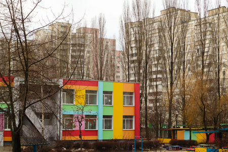 Kiev. Ukraine.January 1, 2022. Colorful bright two-story kindergarten building in courtyard of multi-story apartment buildings. Gray post-Soviet architecture in autumn, winter. Cityscape. Bare trees.のeditorial素材