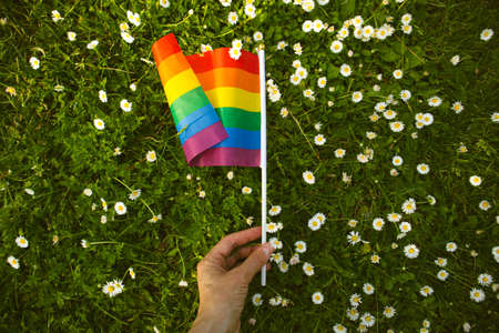 Flag in womans hand against green grass among white flowers. Pride month.の写真素材