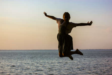 Happy teenage girl 9-12 years old in jumping against a backdrop of blue sea, ocean in summer day. A playful child on summertime vacation. Happy childhood outdoors. Children's Day. Teen girl on the street.の写真素材