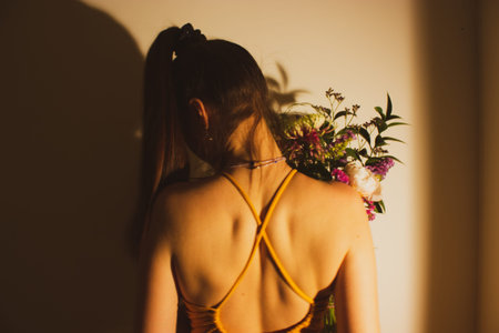 Beautiful girl in open backed dress holding bouquet of flowers back view. Faceless woman in dark...