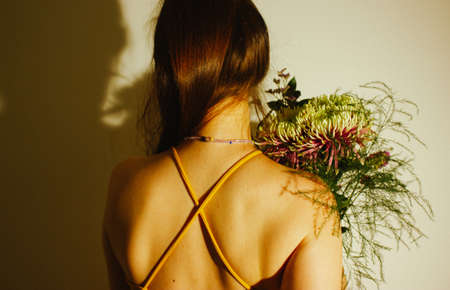 Beautiful girl in open backed dress holding bouquet of flowers back view. Faceless woman in dark shade. Enigmatic lady in summer sundress. female beauty concept. Celebrating holiday, congratulations.の写真素材
