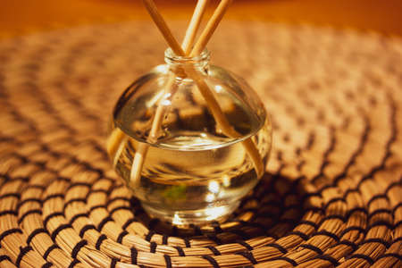 Diffusoria on rattan background. Glass bottle with aroma sticks. Fragrance accessory, home decor. Aroma fragrance reed diffuser. aromatheropy concept. Bottle with scented oil. Perfume for home interiorの写真素材