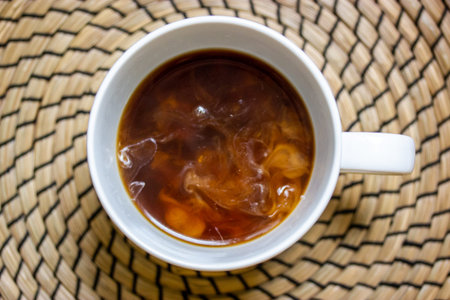 White round cup with black coffee and milk standing on round table on rattan surface top view. A...