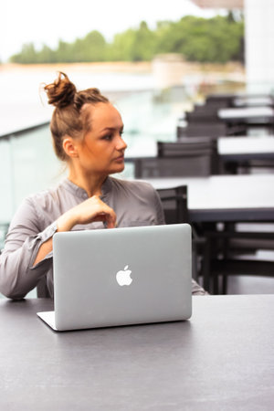 Kyiv, Ukraine. June 7, 2021. Young serious business lady, woman in a gray business suit sits at a table on the terrace of a restaurant cafe with a laptop Apple in focus. working outdoors. remote job.のeditorial素材