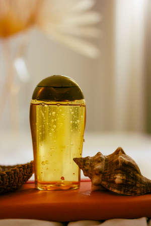 Suntan oil bottle on neutral beige blurred background. Sunblock cosmetics for women body care, a seashell. Natural SPF sunscreen product for summer beach vacations. Lifestyle still life vertical photoの写真素材