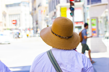 Female traveler, elderly pensioner tourist in straw hat walking down city street on sunny hot summer...