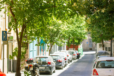 Madrid, Spain. June 1, 2022. Tranquil narrow city street with cars parked on a curb on a sunny...