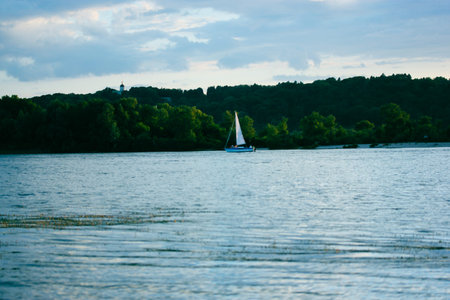 White sailboat sailing on blue calm water surface. water transport. Summer trip, adventure, journey on a river, sea cruise concept. Green trees in national reserve coastline, coast. Nautical landscapeの写真素材