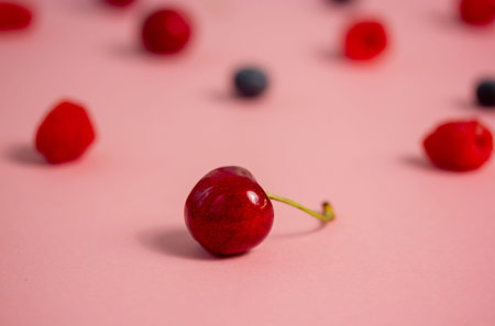 Ripe berries are scattered on a pink table background. Bright red cherry in focus. Delicious ripe berries, cherries, blueberries, strawberries wallpaper. natural antioxidant. Sweet organic fruits.の写真素材