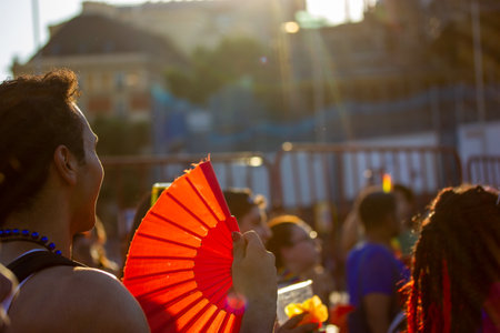 Madrid, Spain. July 9, 2022 Summertime festival, entertainment, outdoor fun. Crowd of people dancing at sunset. A guy with a red fan is having fun, relaxing at a concert in a hot summer day. Pride monthのeditorial素材