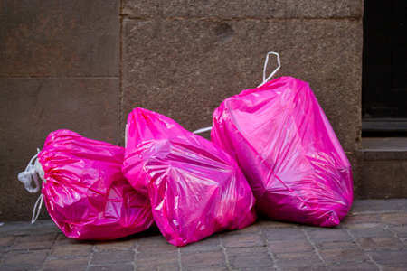 Pile of pink cellophane garbage bags full of garbage trash lie on the sidewalk on a big city street footpath. environmental pollution. urban ecology problems. Plastic rubbish waste sacks recycling.の写真素材