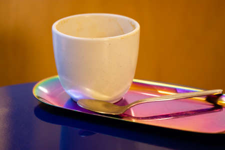 White ceramic cup without handle for cappuccino latte tea stands on stylish pink tray on blue table. Breakfast in a cafe, restaurant. A beautifully chic table set in a coffee shop. Drinkware, teaspoonの写真素材