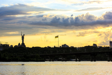 Kyiv, Ukraine. May 1, 2021 A beautiful evening landscape of the Ukrainian capital - silhouettes of the Motherland landmark, the flag of Ukraine against the yellow sky in the evening. Glory to Ukraineのeditorial素材