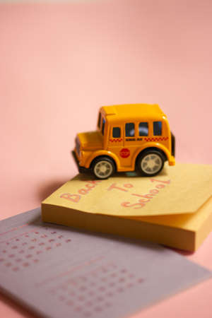 Toy yellow American school bus on table, calendar with dates, colorful wooden pencils lying on pink table. Stationery for studying, drawing, planning. Back to school text on notes. supplies for study.の写真素材