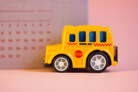 Toy yellow American school bus on violet calendar with dates background is riding on pink table. Stationery for studying, planning. Supplies for study, tools for education. Kids back to school conceptの写真素材