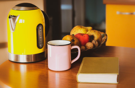 Autumnal still life: pink cup, yellow teapot, bowl of fruit, hardcover book lying on wooden table. Retro and modern housewares, utensils. Reading at cozy sweet home atmosphere. lifestyle concept.の写真素材