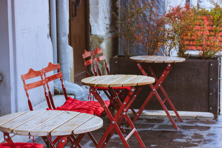 Classic empty cafe restaurant terrace after rain without people. Folding chairs with red soft...