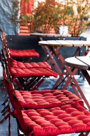 Classic empty cafe restaurant terrace after rain without people. Folding chairs with red soft cushions, wooden round tables on cafeteria patio Garden furniture. Nice area for relaxing on a city streetの写真素材