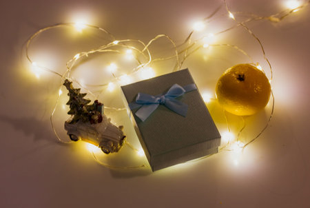 New Year's present in a gift box with a bow, LED lights, tangerine in a dark room top view....