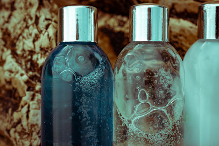 Plastic cosmetic bottles with natural cosmetic in travel containers - shower gel, shampoo with bubbles inside, body lotion in miniature containers against a rock background close up. face body care.の写真素材