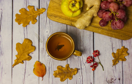Autumnal still life - a cup of tea on a wooden table among the fallen dry oak leaves flatly. Seasonal fruits - grapes, ginger root, agave. fall season. Comfort home, atmosphere of warmth and cozinessの写真素材