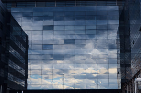 The glass facade of a tall multistory office building, an apartment building with a reflection of...