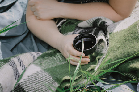 A woman tourist resting in nature at a picnic lying on a green blanket, plaid holding a flask in nature in summer, autumn day. Vintage travel concept.の写真素材