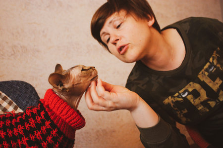 Woman stroking beloved cat Canadian Sphynx breed with a hand. Mistress and bald feline animal in warm red sweater indoors. Human and pet loyalty, affection, trust, real emotions concept World Cats Dayの写真素材