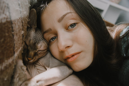 Young brunette girl cuddles, caresses, snuggles with beloved bald Canadian Sphynx breed cat. portrait of cat mistress. Love, affection, tenderness, affection for animals. Feline and woman togethernessの写真素材