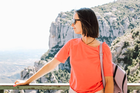 Young beautiful brunette girl with bob-care removed sunglasses in profile. Female tourist travel solo in the mountains. Enjoying trip and breathing in fresh air. Traveling people outdoors on a streetの写真素材