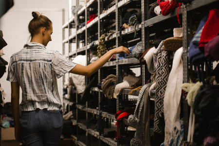Madrid, Spain. September 1, 2022 Young woman walks among rows of shelves of shabby clothes. A girl picks out clothes at a refugee shelter, second hand. Humanitarian aid help to the homeless, destituteの写真素材
