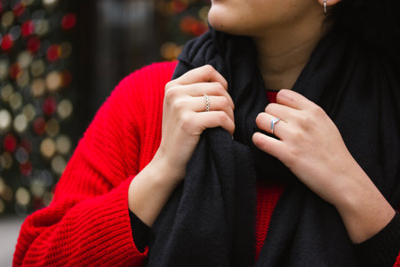 Young girl woman in red knit sweater with black scarf on a cold winter day against decorated Christmas tree toys. Woman's hands with fingers adorned with silver rings. New Year 202の写真素材
