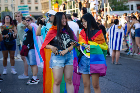 Madrid, Spain. 26 July 2022 Lesbian girls in a rainbow flag, symbol of LGBT community at a gay parade in summer day. Pride month party celebration on a city street. People with bright flags outdoors.のeditorial素材