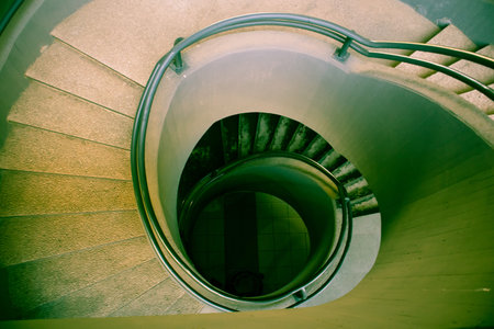 A spiral staircase, stone or concrete steps leading down and metal handrails. Brutalist architecture...