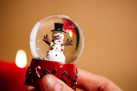 New Year's glass toy snow globe with snowman inside and snowflakes falling in a hand. Home decor, candles gift for winter holidays. Cozy Christmas atmosphere. happy new year 2023 celebration wallpaperの写真素材