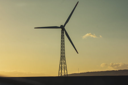 Silhouette of wind turbine, windmill with huge propeller in a field against sunset sky....
