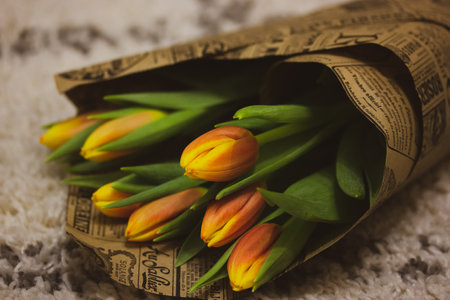 Bouquet of yellow and orange tulips wrapped in paper wrap. Fresh spring summer bulb flowers lying on a tufted rug in a cozy home atmosphere. Floral present, gift for mother, beloved in March 8.の写真素材