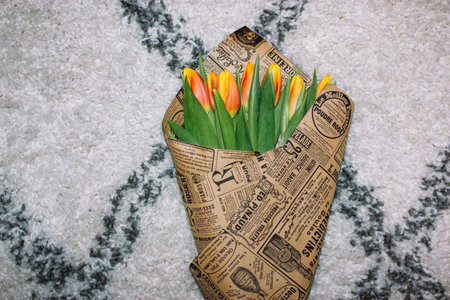 Bouquet of yellow and orange tulips wrapped in paper wrap. Fresh spring summer bulb flowers lying on...