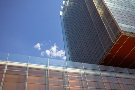 Modern tall building with glass facade against blue sky in sunny day. Office building of a company...