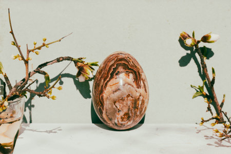 Easter egg with natural brown stone texture on green background Spring still life with blooming tree branches white flowers. Cinematic vintage authentic Easter holiday concept photo Springtime holidayの写真素材