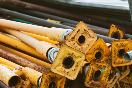 Old scaffold tubes are stored outside in a pile. Different yellow tube baseplates. Parts of the...
