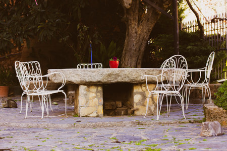 Large round stone table on a beautiful terrace, patio. Place to relax outdoor in a backyard in the English garden without people. French style vintage white metal chairs. potted flowers. sleeping catsの写真素材