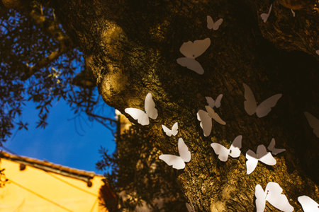 White paper decorative butterflies decorate the trunk of an old tree. origami hobby. easter holidays decor. Creative idea for decorating trees. abstract art ideas. Spring season nature awaking.の写真素材